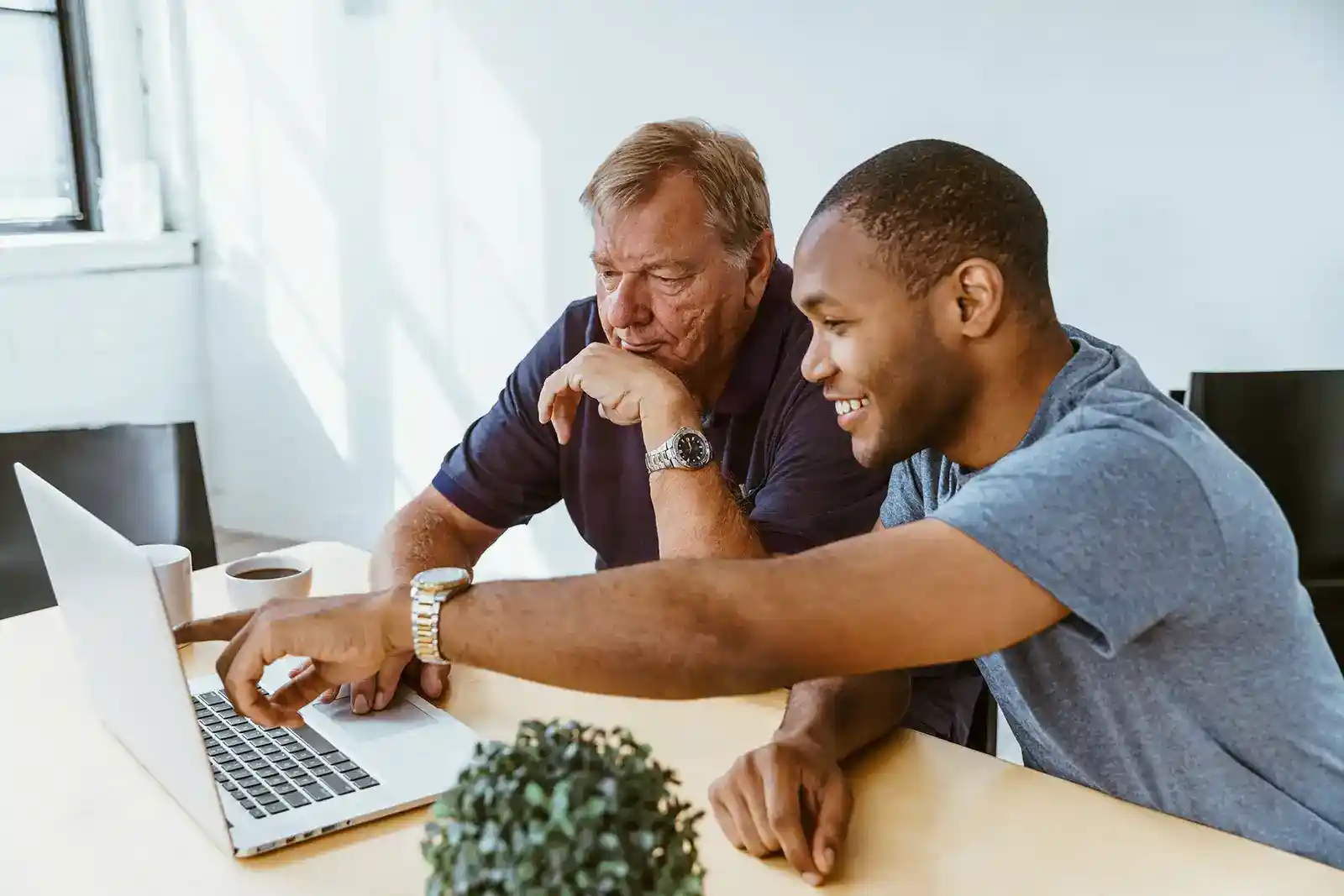 A man helping an older man by a computer screen.